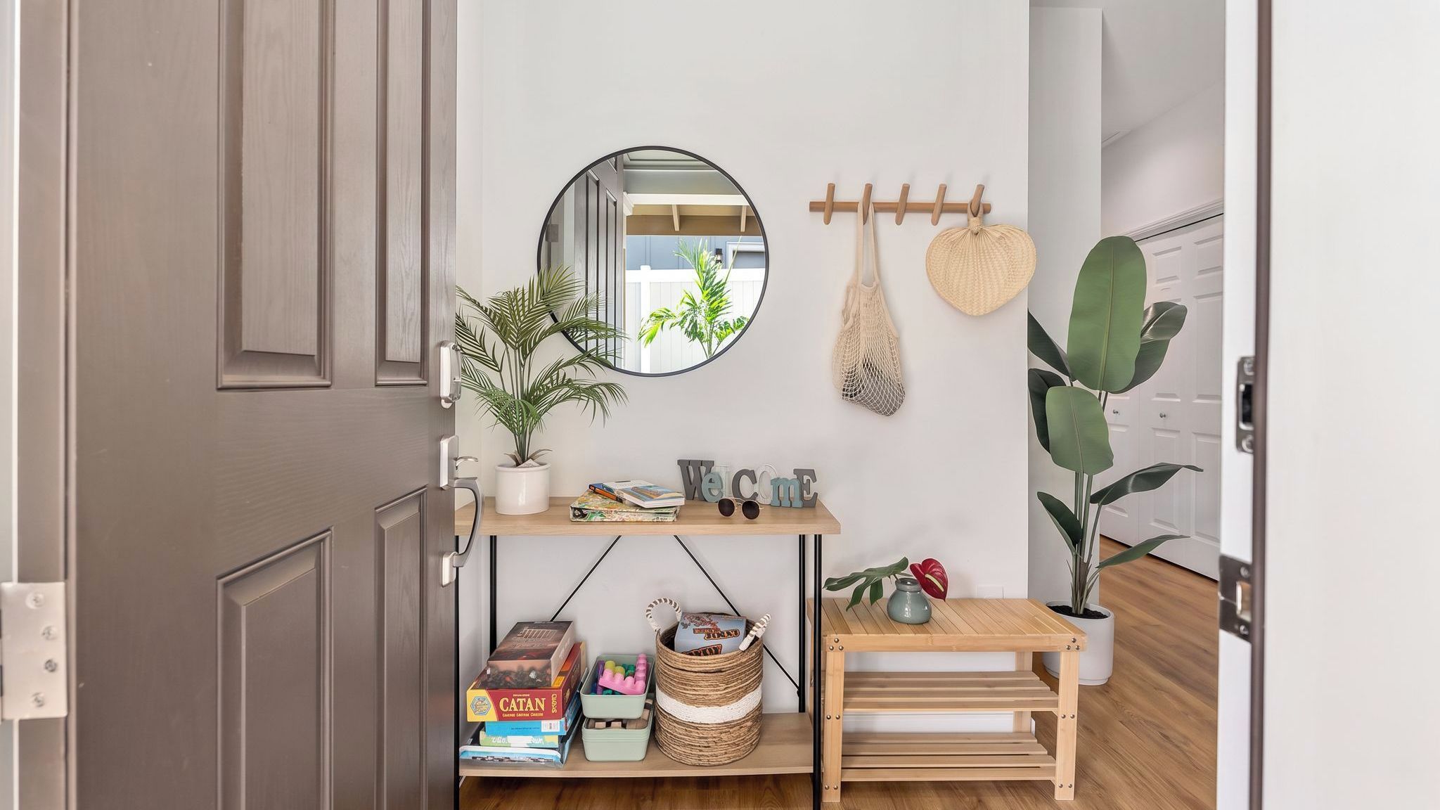 Une pièce avec une porte en bois, un miroir rond, une pancarte de bienvenue, une petite table en bois et une plante en pot.