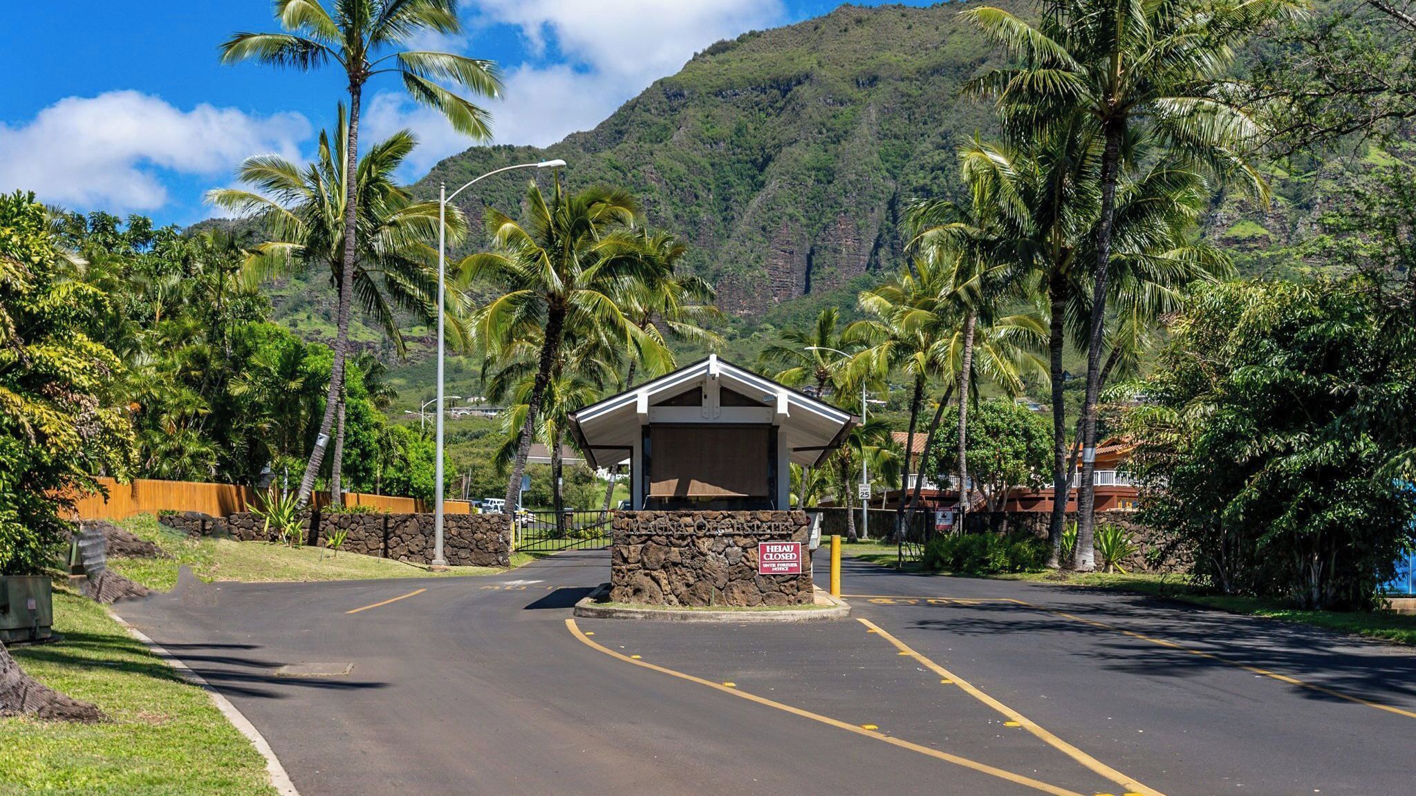 A closed building with a stone base and a small roof, surrounded by palm trees and a mountainous backdrop.