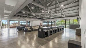 Un espacio interior amplio con techo alto, ventanas grandes y una zona de bar con asientos.