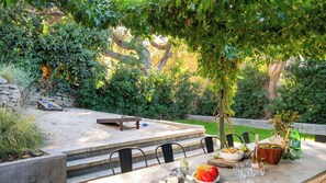 Un área de comedor al aire libre con una mesa preparada para dos personas, rodeada de follaje y un muro de piedra.