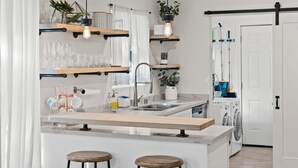 Eine moderne Küche mit einer zentralen Kochinsel, Barhocker, hängenden Regalen und einer Waschmaschine.