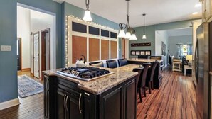 A kitchen with a central island, wooden flooring, pendant lighting, and a view into the dining area.