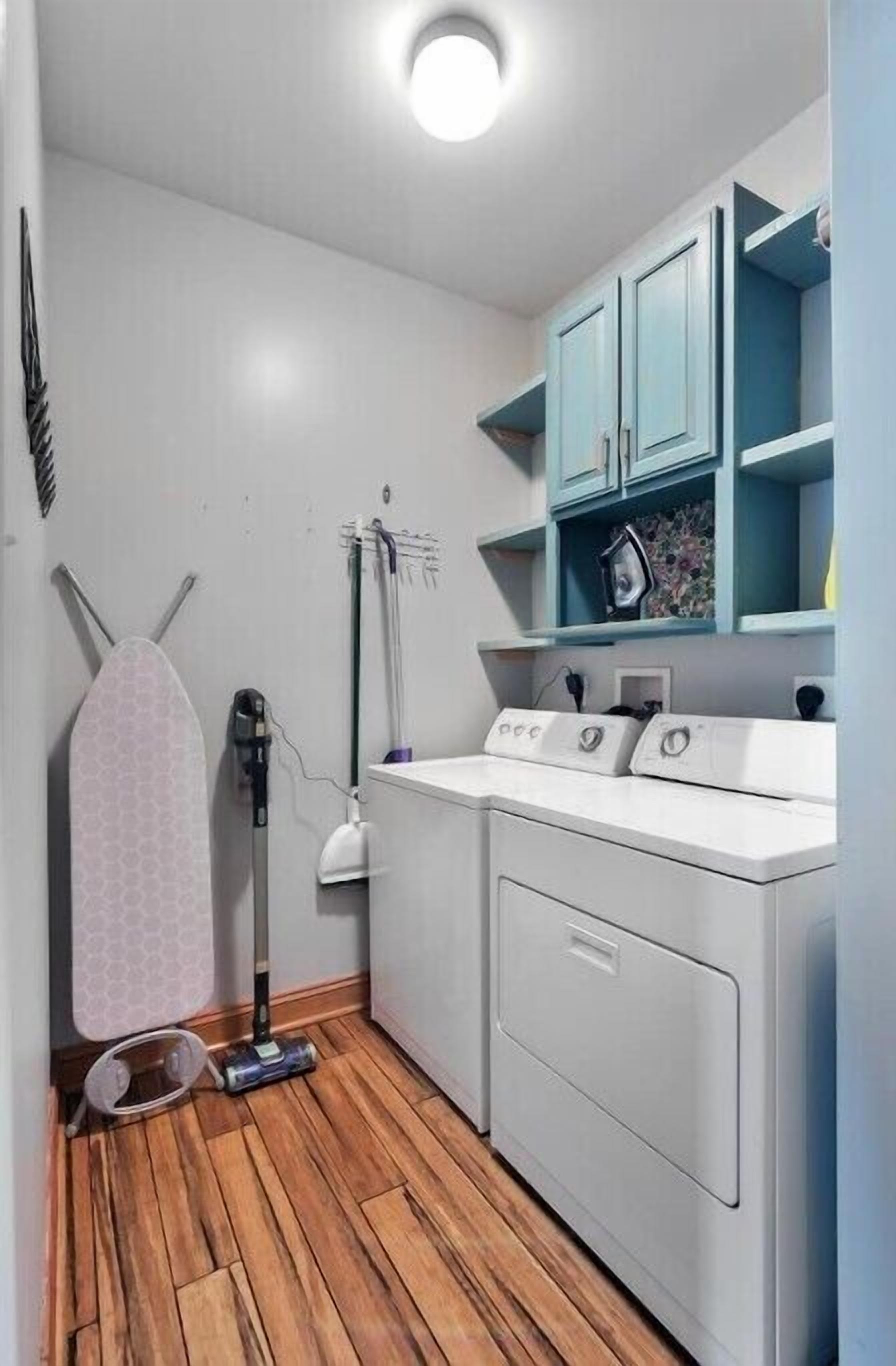 A laundry room with a washing machine, dryer, ironing board, and a vacuum cleaner.