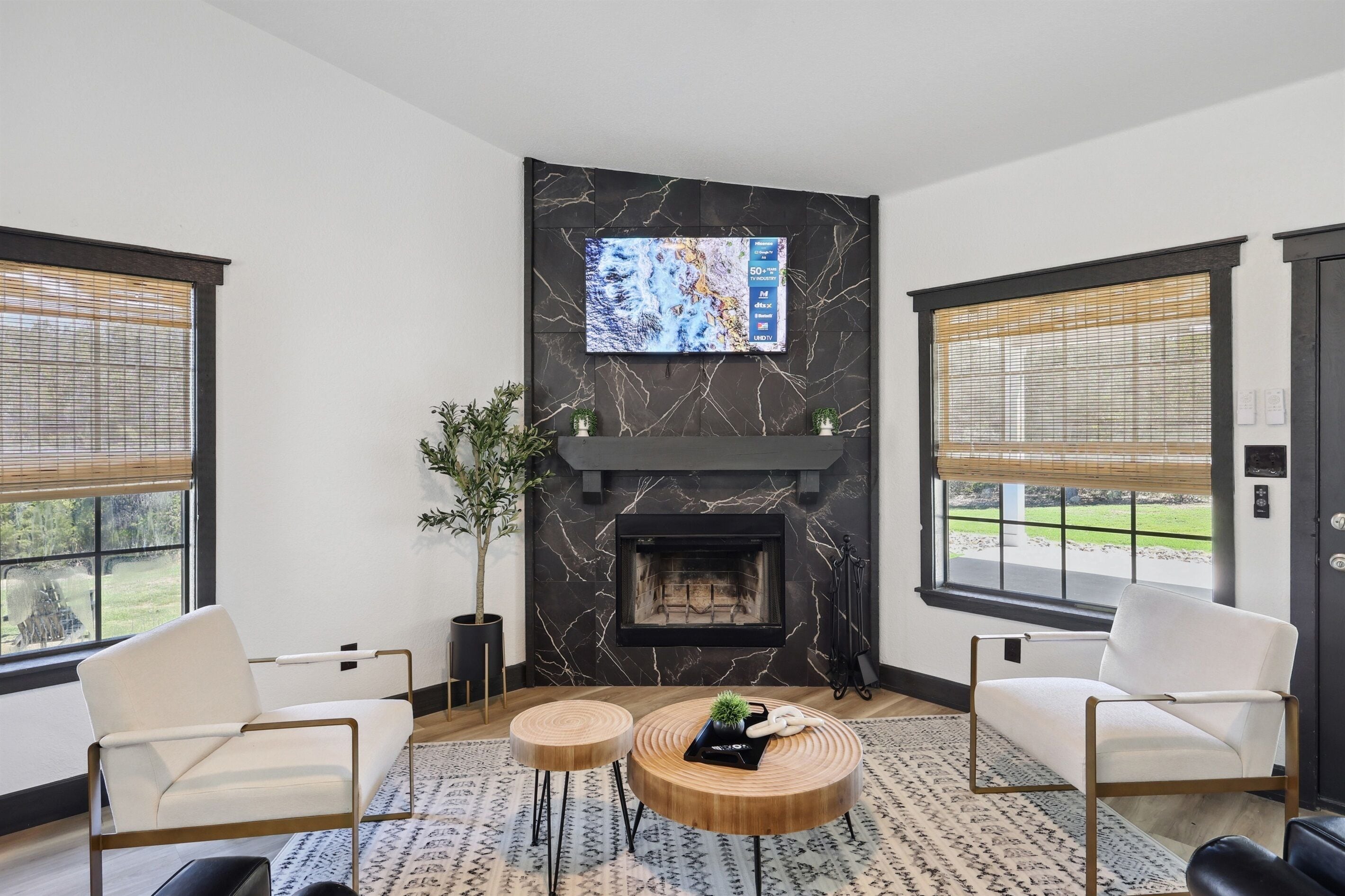 Una sala moderna con chimenea, dos sillones blancos, una mesa de centro y un televisor montado en una pared de mármol.