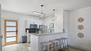 A modern kitchen with white cabinets, a stainless steel refrigerator, and a central island with bar stools. - The Retreat 20: Lake Daze (Graford)