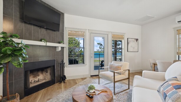 A modern living room with a fireplace, white sofas, a coffee table, and a large TV mounted on the wall. - The Retreat 20: Lake Daze (Graford)
