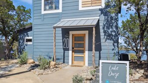 A blue building with a wooden door and number 20, surrounded by desert landscaping. - The Retreat 20: Lake Daze (Graford)