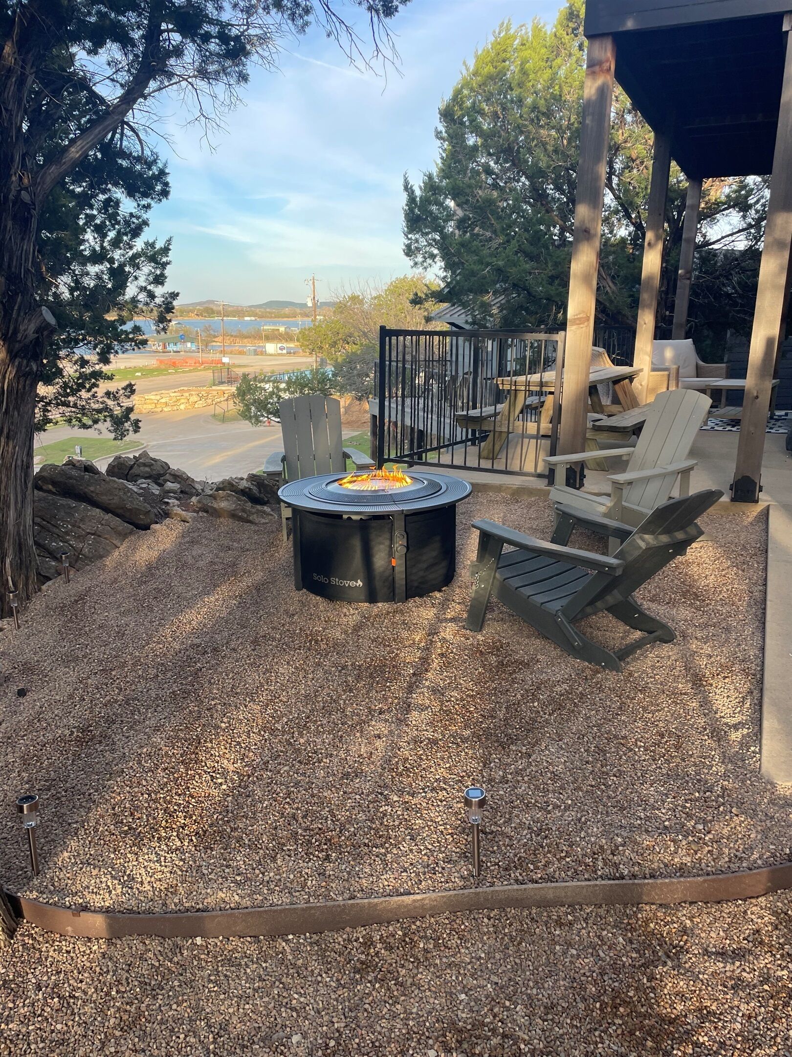 A patio area with a Solo Stove fire pit, Adirondack chairs, and a view of a road and distant landscape.