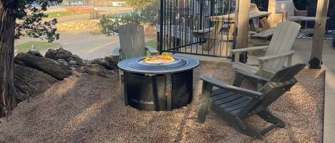 A patio area with a Solo Stove fire pit, Adirondack chairs, and a view of a road and distant landscape.