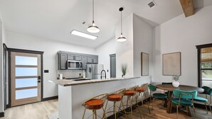 A modern kitchen with bar stools, a dining table, and pendant lighting. - Cabin 7: Sweetest Escape (Graford)