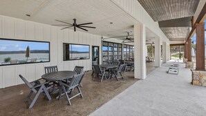A covered outdoor dining area with tables and chairs, large windows with views of the water, and ceiling fans. - Cabin 7: Sweetest Escape (Graford)