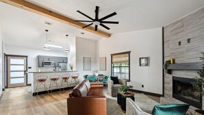 A spacious living room with a fireplace, a kitchen in the background, and a dining area with chairs. - Cabin 7: Sweetest Escape (Graford)