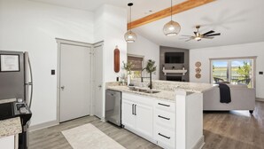 A modern kitchen with white cabinetry, a built-in dishwasher, pendant lighting, and a large window offering a view of the outdoors.