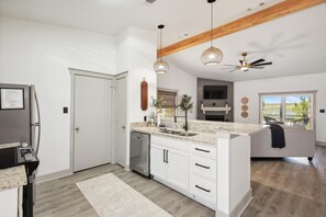 A modern kitchen with white cabinetry, a built-in dishwasher, pendant lighting, and a large window offering a view of the outdoors.