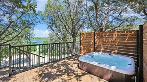 A hot tub on a wooden deck with a view of a lake and trees.