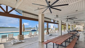 An outdoor pool area with lounge chairs, wooden tables, and ceiling fans.
