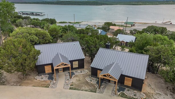 A lakeside property with two cabins featuring metal roofs and wooden accents, surrounded by trees and a view of a calm lake.