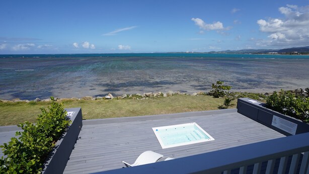 Een terras met een jacuzzi met uitzicht op een heldere blauwe zee en verre bergen.