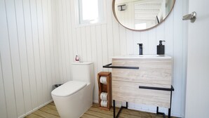Een badkamer met een toilet, een houten wastafelmeubel met een spiegel en een klein houten krukje.