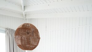 Een slaapkamer met een groot bed, een nachtkastje, een hanglamp en een raam met gordijnen.