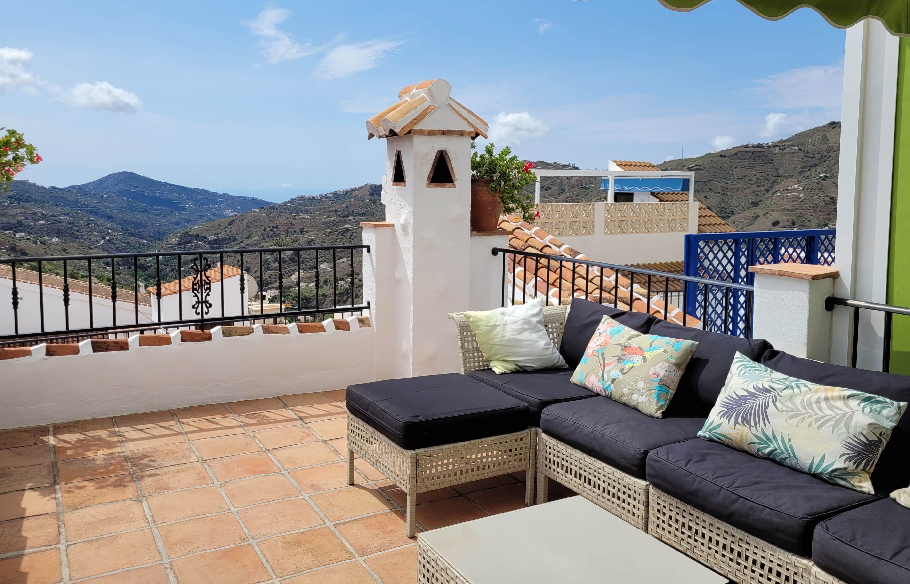 A balcony with a wicker sofa, a small table, and a view of the countryside.