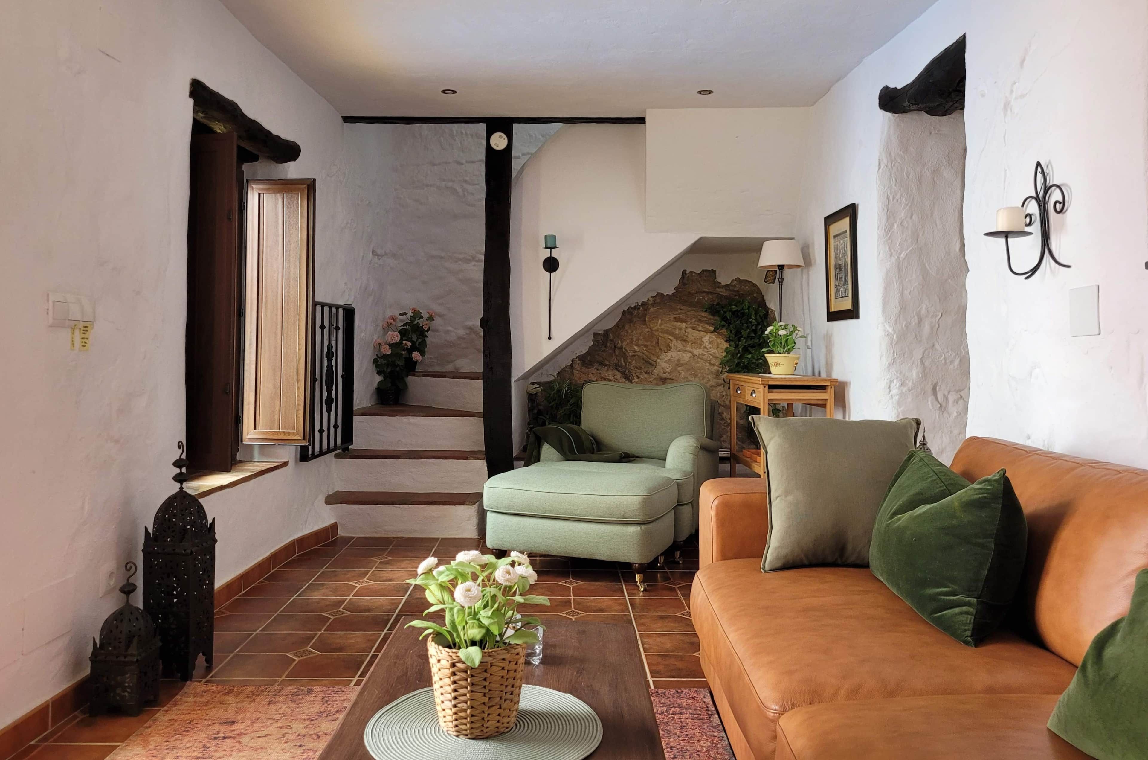 Una sala de estar con un sofá, una mesa de centro con una planta, una escalera con un muro de piedra y una lámpara en la pared.