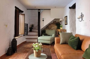 Un salon avec un canapé, une table basse ornée d’une plante, un escalier avec un mur en pierre et une lampe fixée au mur.