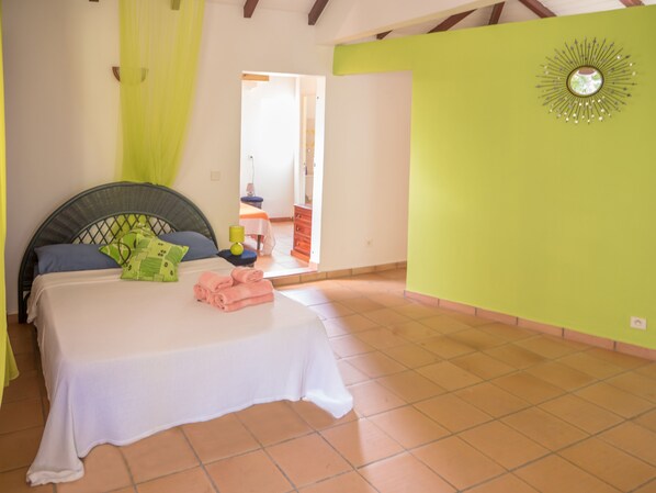 Een slaapkamer met een bed, kussens, een nachtkastje en een groene muur met een decoratieve spiegel.