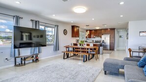 Een moderne woonkamer met een flatscreen televisie, een eethoek met een houten tafel en stoelen, en een keuken op de achtergrond.