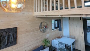 Un intérieur moderne avec un plafond en bois, un balcon de style industriel, un coin repas et un espace détente avec des coussins.