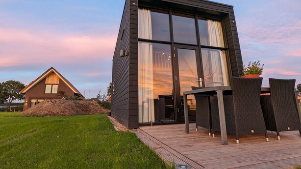 Une maison moderne dotée d’une grande baie vitrée, d’une terrasse en bois et d’un petit espace de détente extérieur.