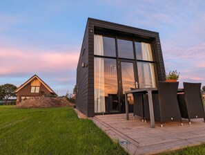 A modern house with a large glass window, a wooden deck, and a small outdoor seating area.
