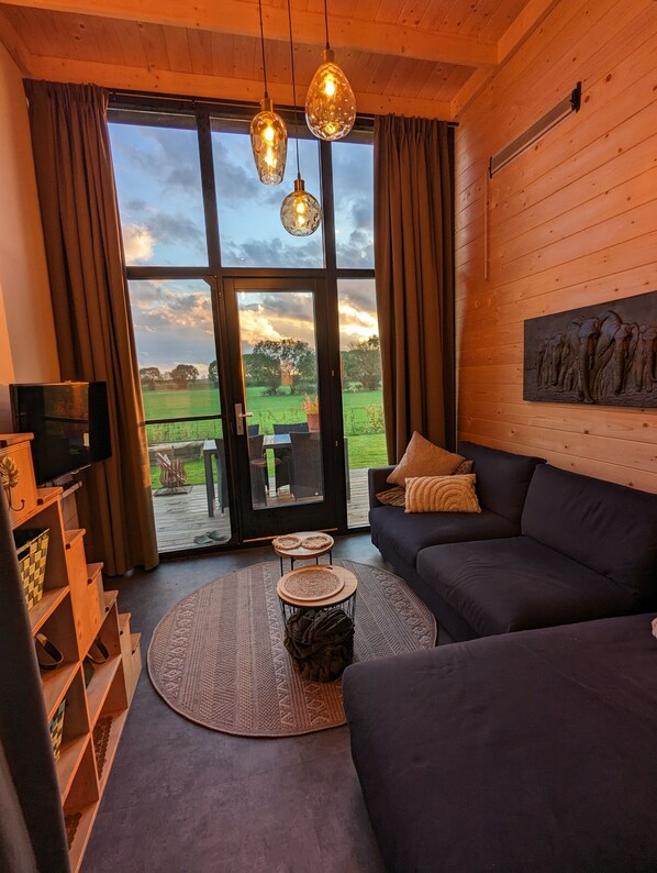 A cozy living room with a dark sofa, a television, and a large window with curtains.