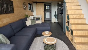 Un espace de vie moderne de style loft, avec un canapé d’angle bleu foncé, une table basse ronde et un escalier à marches en bois.