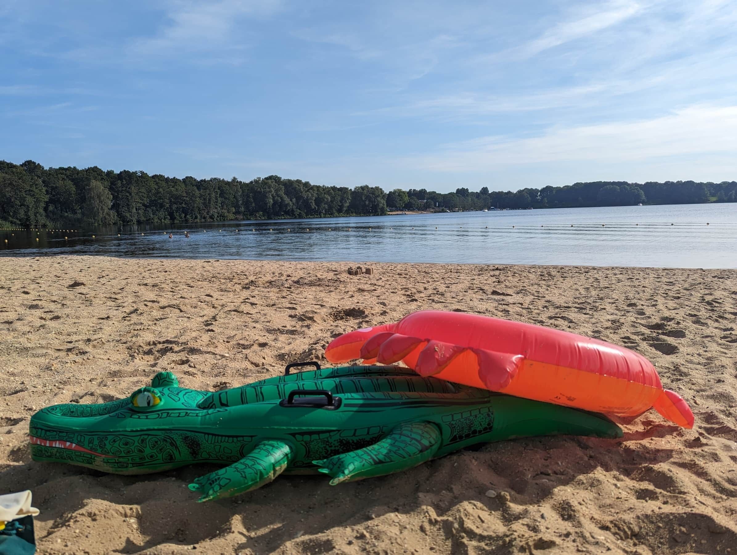 A beach with a green inflatable toy and a red inflatable toy on the sand.