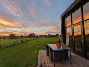 A deck with a table and chairs, overlooking a grassy field and a sunset sky.