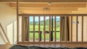 Une pièce dotée d’une grande fenêtre, de poutres apparentes en bois au plafond et offrant une vue sur un paysage verdoyant.