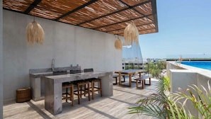 A modern outdoor kitchen with a stone countertop, wooden stools, and a pergola overhead. - Kasa Kolibri 2 bedroom apartment in Aldea Zama close to beach (Tulum Quintana Roo)