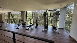 A gym with various exercise machines, large windows, and a wooden floor. - Kasa Kolibri 2 bedroom apartment in Aldea Zama close to beach (Tulum Quintana Roo)