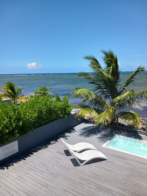 En träveranda med en pool, palmer och utsikt över havet.