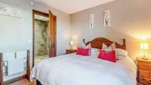 Een slaapkamer met een groot bed, een houten hoofdbord, twee nachtkastjes met lampen, een houten stoel en een douche.