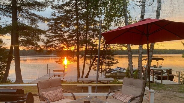 A deck with outdoor furniture, a fire pit, and a view of a sunset over a body of water. - Anna Bananas Beachfront Bungalow (Hazelhurst)