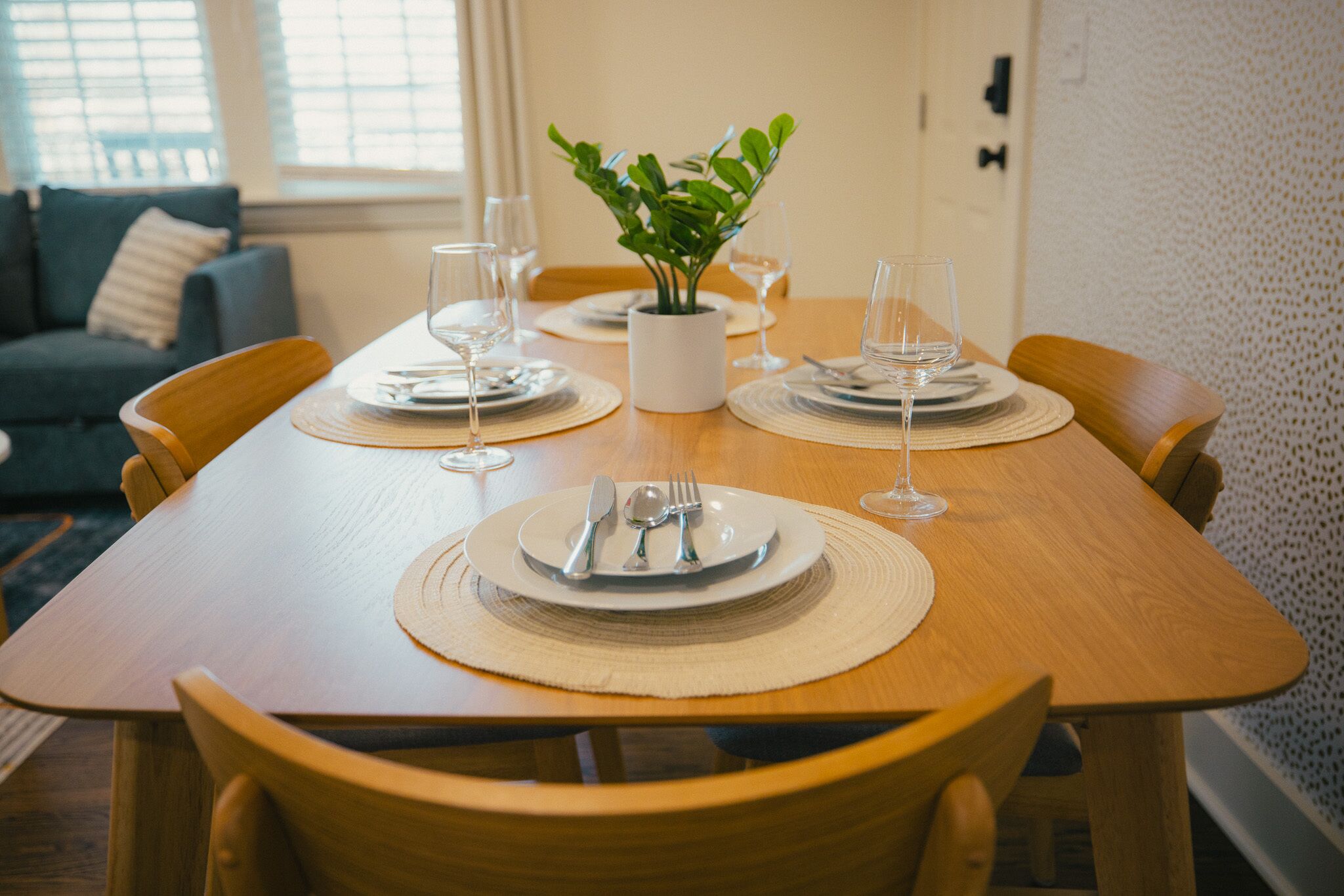 Una mesa de comedor dispuesta con platos, cubiertos y vasos, rodeada de sillas de madera.