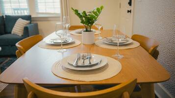 Una mesa de comedor dispuesta con platos, cubiertos y vasos, rodeada de sillas de madera.