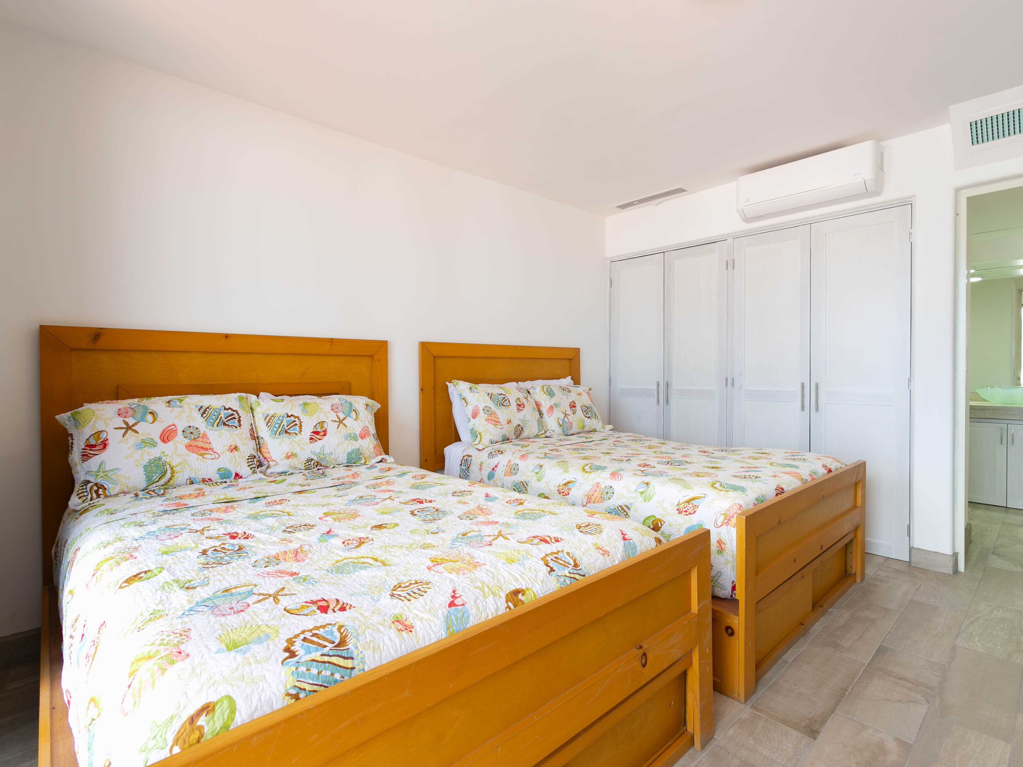 Une chambre à coucher avec deux lits en bois, une armoire et une salle de bain visible à travers une porte ouverte.