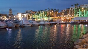 Ein Yachthafen mit vertäuten Booten, eine Uferpromenade und Gebäude mit beleuchteten Schildern.