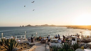 Ein Küstenrestaurant mit Terrassenplätzen und Meerblick, inklusive einer Ansicht ferner Inseln und einem klaren Himmel.