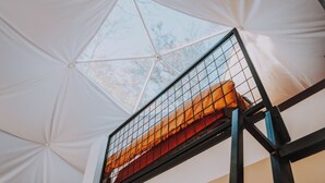 A room with a high ceiling and a large window, a bed with a headboard, and a small round mirror on the wall. - Mockingbird Geodesic Dome at Starlight Haven Resort (Hot Springs)