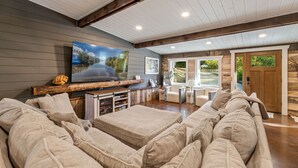 Un salón espacioso con un sofá modular grande, un televisor de pantalla plana montado en la pared y un mueble de entretenimiento de madera.