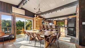 Un comedor espacioso con una gran mesa de madera y sillas, una araña y vistas al exterior.